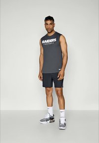 Camiseta atlética cinza sem mangas com o texto "RAIDERS" e "futebol"; combinada com calções escuros e sapatilhas cinzas. Design minimalista e desportivo.