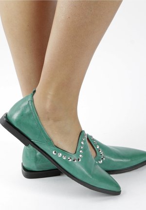 Vihreät nahkakengät, joissa on terävät kärjet, hopeiset niittikoristeet yläreunassa ja matala musta pohja, leikkauskuvioinnilla.