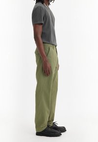 Grå bomullströja, gröna bomullsbukser och svarta skor. Byxorna har sidofickor och en avslappnad passform. Enkelt mönster, inga dekorationer eller accenter.