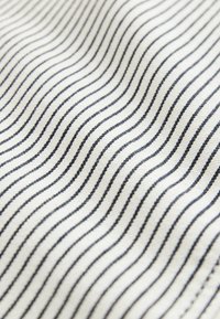 Baumwollstoff mit einer welligen Textur, der abwechselnd weiße und marineblaue Streifen aufweist und ein rhythmisches Muster erzeugt.