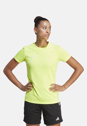 T-shirt de sport jaune vif à manches courtes, avec des accents texturés sur les épaules et un détail de logo. Porté avec un short noir.