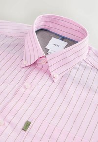 Cămașă roz cu dungi verticale fine, guler cu nasturi și buzunar aplicat. Are nasturi din plastic și etichetă de brand în interior.
