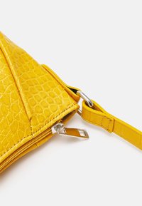 Geel lederen tas met een textuurafwerking, diagonale vorm, ritssluiting en een afneembare strap met metalen hardware.