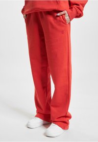 Røde, løstsiddende sweatpants med sidelommer og let broderet detalje, parret med hvide sneakers på en neutral baggrund.