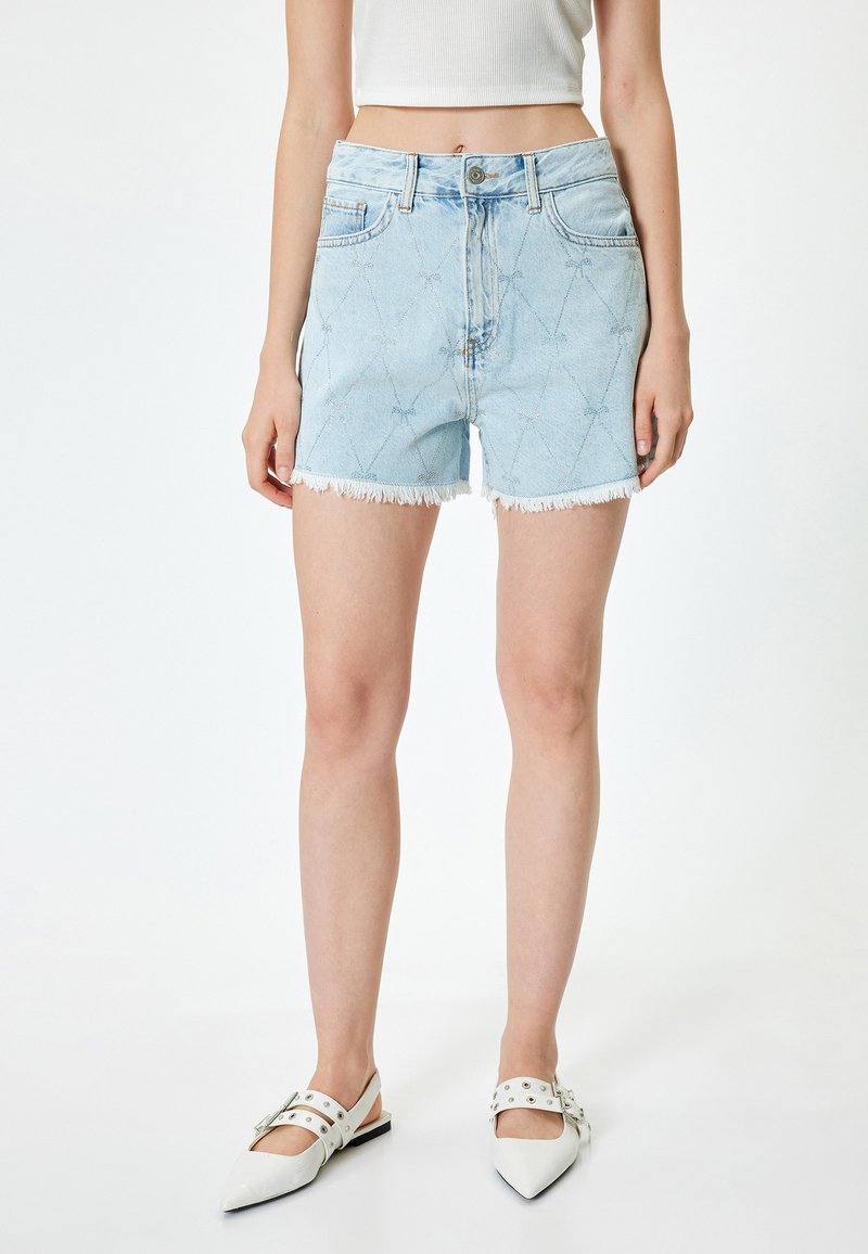 Shorts de mezclilla azul claro con dobladillo deshilachado, que presentan un patrón de diamantes y un diseño de cinco bolsillos. Combinados con zapatos planos blancos de punta.