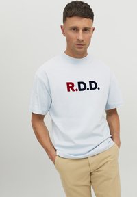 Vaaleansininen puuvillapaita, jossa on rohkeasti painettu "R.D.D." -logo punaisena ja tummansinisenä. Lyhyet hihat, rento malli ja pyöreä kaula-aukko.