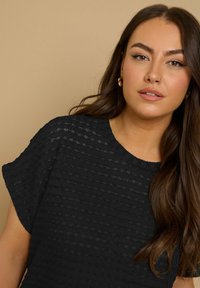 Black textured top featuring a ribbed design, short sleeves, and a round neckline, with a smooth finish and subtle sheen.