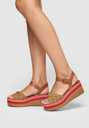 Brown leather wedge sandals with woven straw upper, featuring a crisscross design, topped with a red and natural woven sole.