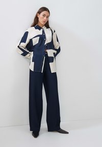 Navy and cream patterned button-up shirt with a collar, paired with wide-leg navy trousers and pointed black shoes. Smooth fabric texture.