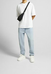 Camiseta blanca de manga corta, jeans de mezclilla azul claro y zapatillas blancas. Se lleva un bolso negro cruzado sobre el hombro, añadiendo funcionalidad.