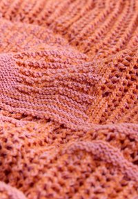 Strikket stof i forskellige nuancer af pink og orange, med et tekstureret mønster med åbne masker og glatte områder, der skaber visuel kontrast.