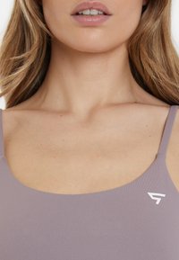 Light purple fitted tank top with narrow straps, made from soft ribbed material. Features a small white logo on the left side.