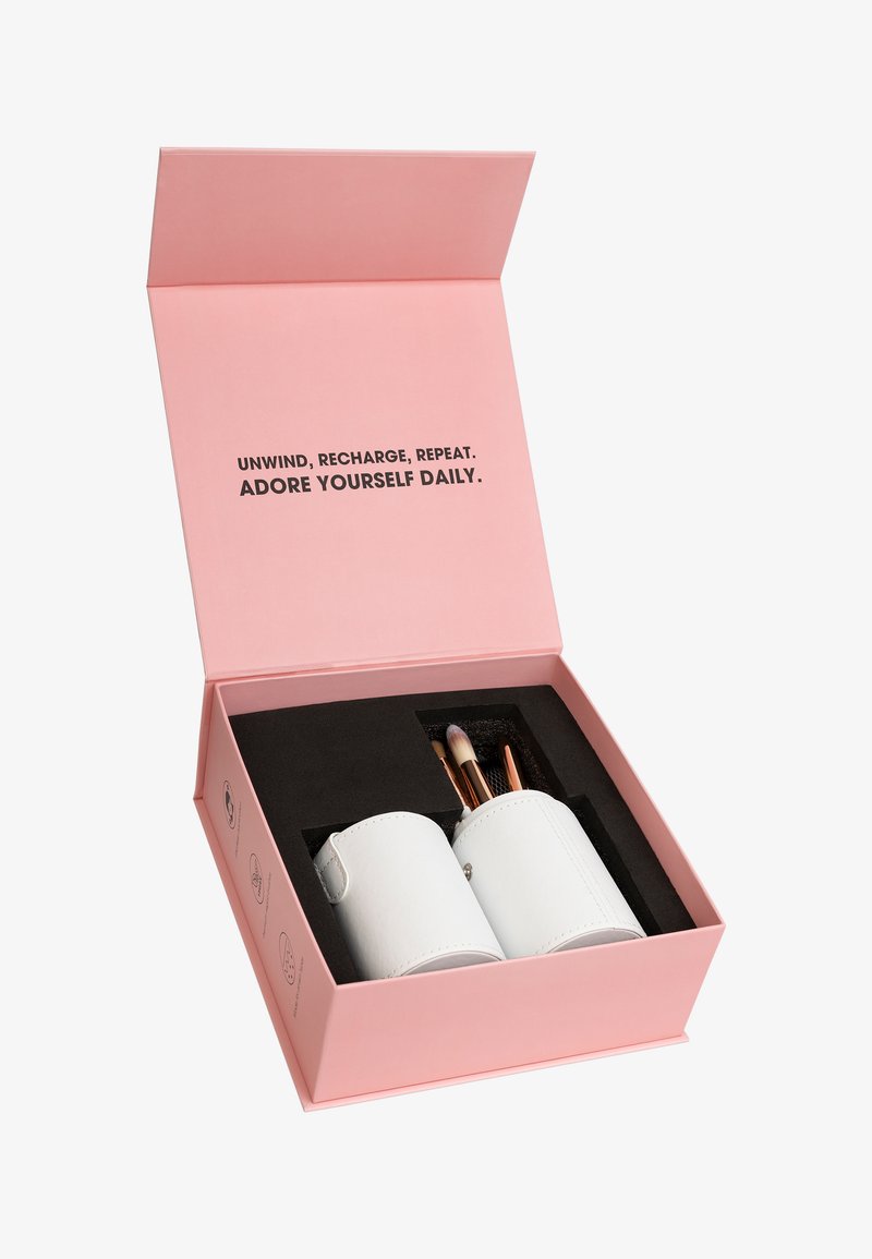 Roze doos met motiverende tekst aan de binnenzijde van het deksel en twee witte houders met make-upborstels op een zwarte schuiminzet.