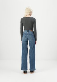 Top gris de manga larga con cuello redondo, combinado con unos vaqueros azules de cintura alta y pierna ancha. Los vaqueros cuentan con bolsillos traseros y una etiqueta de cuero.