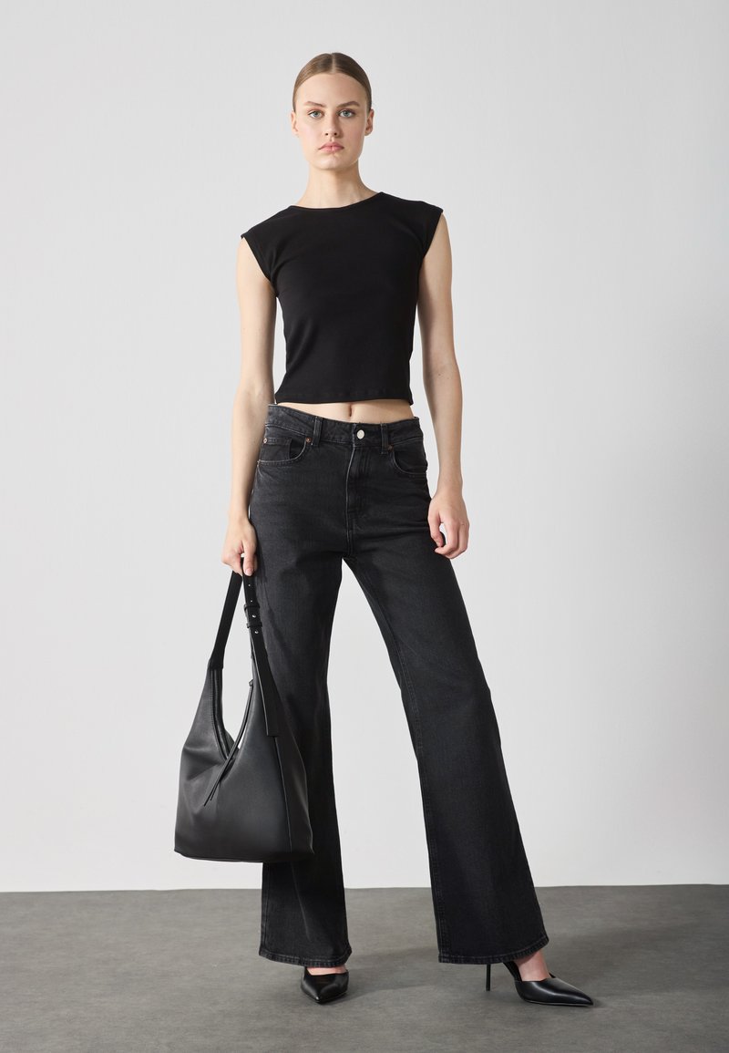 Camiseta negra recortada con mangas tipo cap, combinada con unos jeans negros de pierna ancha y cintura alta. Incluye un bolso de cuero negro texturizado y unos zapatos de tacón de punta.