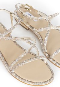 Płaskie sandały z beżową skórzaną wkładką, z krzyżującymi się paskami ozdobionymi błyszczącymi cyrkoniami oraz małym słupkowym obcasem.