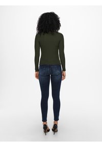 Haut à manches longues côtelé vert olive avec ourlets festonnés, associé à un jean skinny bleu foncé et des chaussures à talons noirs.