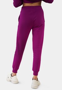 Lila Jogginghose mit weichem Material, elastischem Bund und schmal zulaufenden Bündchen, kombiniert mit weißen Sneakers. Keine sichtbaren Muster oder Akzente.