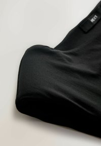 Černá tkanina s hladkým povrchem, zavěšená v nerovném tvaru, s minimálním šitím a štítkem na okraji pro branding.