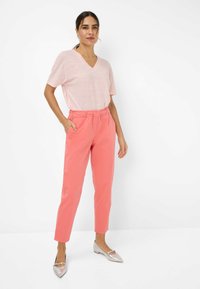 Lichtroze V-hals T-shirt gecombineerd met koraalkleurige broek met koordjes. Model draagt metallic platte schoenen. Zachte textuur, casual pasvorm.
