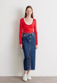 Rød langermet topp med hvit hals, sammen med en blå denim midi-skjørt med en frontslitt, akkompagnert av hvite joggesko.