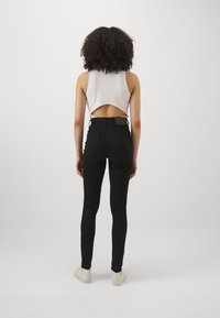 Fekete, magas derekú skinny farmernadrág, szűk fazonnal, világos színű, ujjatlan felsővel párosítva, amelynek kivágott hátrész dizájnja van.