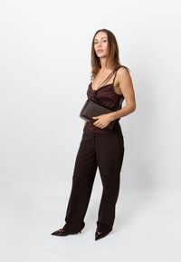 Geantă de mână maro închis cu finisaj texturat, formă dreptunghiulară și curea scurtă, purtată de un model îmbrăcat într-o ținută maro asortată.