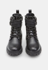 Stivali alla caviglia neri in pelle con punta tonda, fibbie decorative e lacci. Presentano una superficie testurizzata e suole in gomma robuste.