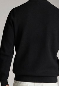 Pull noir doté d'un col rond, de poignets et d'un ourlet côtelés, avec une texture lisse et une coupe ajustée, présenté de dos.