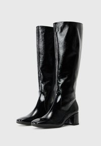 Botas pretas até ao joelho feitas de material sintético brilhante, com bico quadrado e salto em bloco. Textura suave com detalhes de costura vertical.