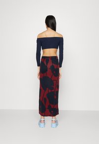 Top bez ramínek námornické modré barvy s dlouhými rukávy, doplněný o sukni s vysokým pasem v červené barvě se květinovým vzorem a tmavými siluetami, ve střihu do písmene A.