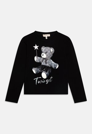 Chemise noire à manches longues avec un ours en peluche à motifs tenant une baguette étoilée et portant un tutu noir, étiquetée Twinset sous l’ours.