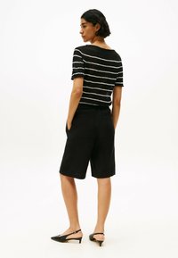 Top corto a maniche corte a righe nere con una vestibilità ampia, abbinato a pantaloni corti neri al ginocchio. Le scarpe sono décolleté slingback nere con punta affusolata.