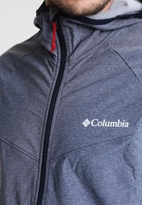 Gray Columbia jacket with a high collar, featuring a full zipper and red pull tab. Logo displayed on the front in white.
