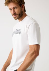 T-shirt bianco in cotone con una grafica testurizzata nera che legge "ISSUES", maniche corte e vestibilità rilassata.
