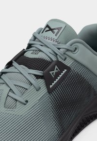 Krupan plan sportske cipela svijetlo tirkizne boje s teksturiranim materijalom, crnim akcentima i vezicama isprepletenim s sustavom za skrivanje vezica.