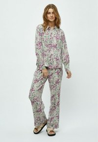 Pajama set s cvetlično prints, ki vključuje srajco na gumbe s ovratnikom in dolgimi rokavi, v kombinaciji z ohlapnimi hlačami, vse v zelenih, roza in belih odtenkih.