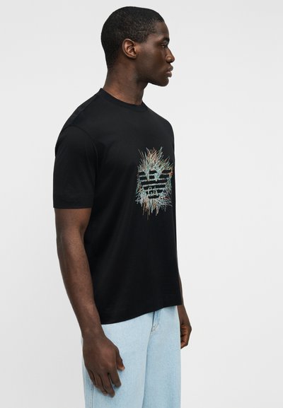 Μαύρο κοντομάνικο μπλουζάκι με πολύχρωμο γραφικό σχέδιο στο στήθος. Το ύφασμα φαίνεται λείο με κλασικό στρογγυλό λαιμό.