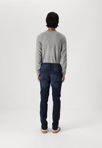 Grå långärmad skjorta med ett strukturerat mönster och raglanärmar, kombinerad med mörkblå jeans och ljusa skor. Ingen synlig märkning.