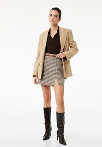 Beige blazer over en brun polo, parret med en houndstooth mini nederdel med en sideslids og brun bælte. Sorte knæhøje støvler med hæl.