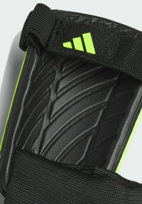 Espinillera de fútbol negra con superficie texturizada y acentos verdes. Correa elástica ajustable para un ajuste seguro. Diseño duradero y contorneado.
