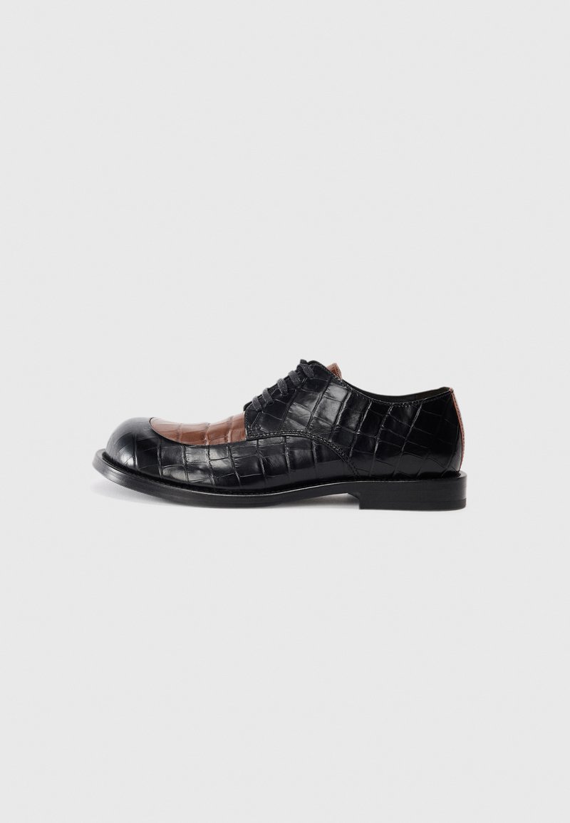 Black and brown crocodile-embossed leather shoe with a rounded toe, lace-up front, and flat sole. Features contrasting texture and colors.