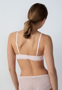 Soutien-gorge rose clair avec des détails en dentelle, des bretelles réglables et une fermeture à crochets. Texture lisse avec des bords décoratifs.