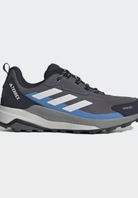 Μαύρο και γκρι παπούτσι πεζοπορίας Adidas Terrex με λευκές ρίγες, μπλε λεπτομέρεια, παχιά σόλα και μαύρα κορδόνια σε λευκό φόντο.