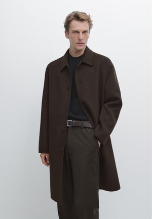 Brown wool overcoat with a collared neckline, front buttons, and side pockets, paired with a black top and dark trousers.