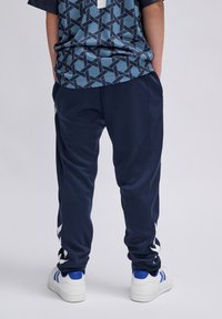 Marineblauwe sport joggers hebben taps toelopende benen, witte zijaccenten, een elastische tailleband en een gladde textuur, gekoppeld aan een gestreept blauw shirt.