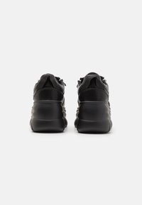 Baskets noires avec une semelle épaisse et sculptée, dotées d'une tige en cuir lisse, d'accents en mesh et de détails discrets avec fermetures éclair sur les côtés.