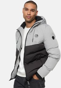 Chaqueta de plumas gris y negra con capucha, con cierre de cremallera, logo en el pecho y puños elásticos. Diseño acolchado texturizado con bolsillos.
