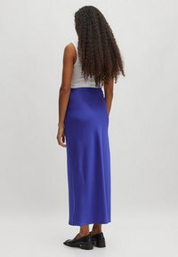 Satijnen blauwe maxi-jurk met een gladde textuur. Heeft een slim fit met een tailleband. Gecombineerd met zwarte schoeisel. Achteraanzicht weergegeven.