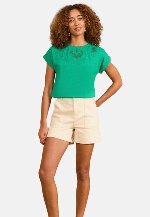 Green short-sleeve top with embroidered detailing, paired with beige shorts. The top has a rounded neckline and relaxed fit, made of a lightweight material.
